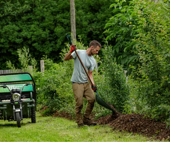 Un jardinier utilisant une pelle pour étaler du broyat au pied des haies au Jardin des Partages, illustrant l'entretien des sols et la promotion de la biodiversité à la Vallée de la Millière.