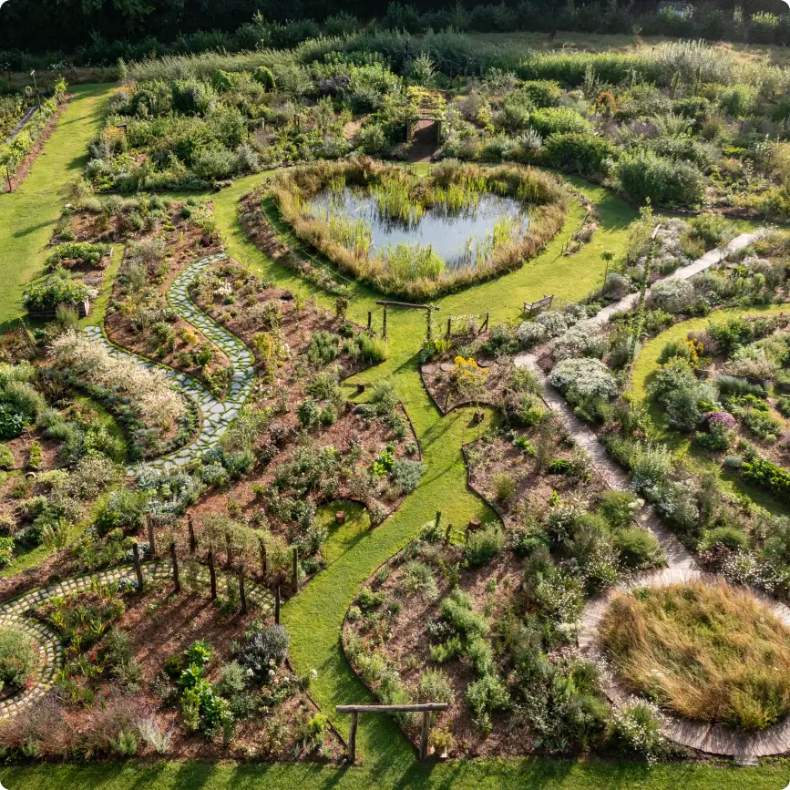 Vue aérienne du Jardin des Partages à la Vallée de la Millière, montrant le bassin central en forme de cœur entouré de sentiers sinueux et de parcelles végétalisées.