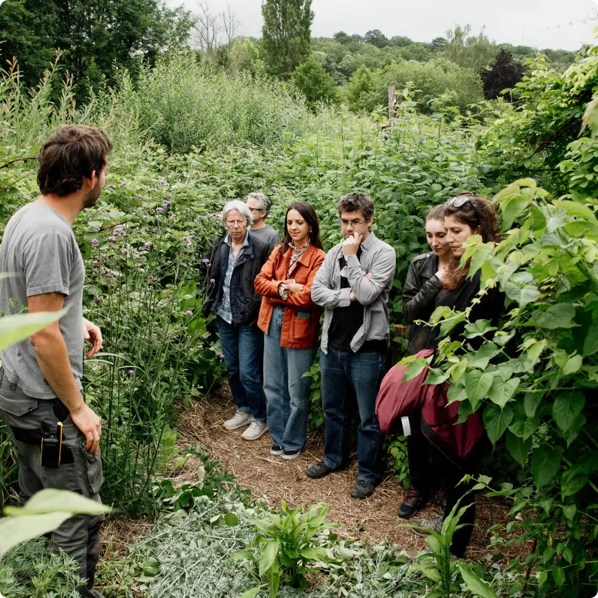 Un groupe de visiteurs attentifs lors d'une session de pédagogie en plein air au Jardin des Partages à la Vallée de la Millière, illustrant la transmission des connaissances sur la biodiversité et le réensauvagement.