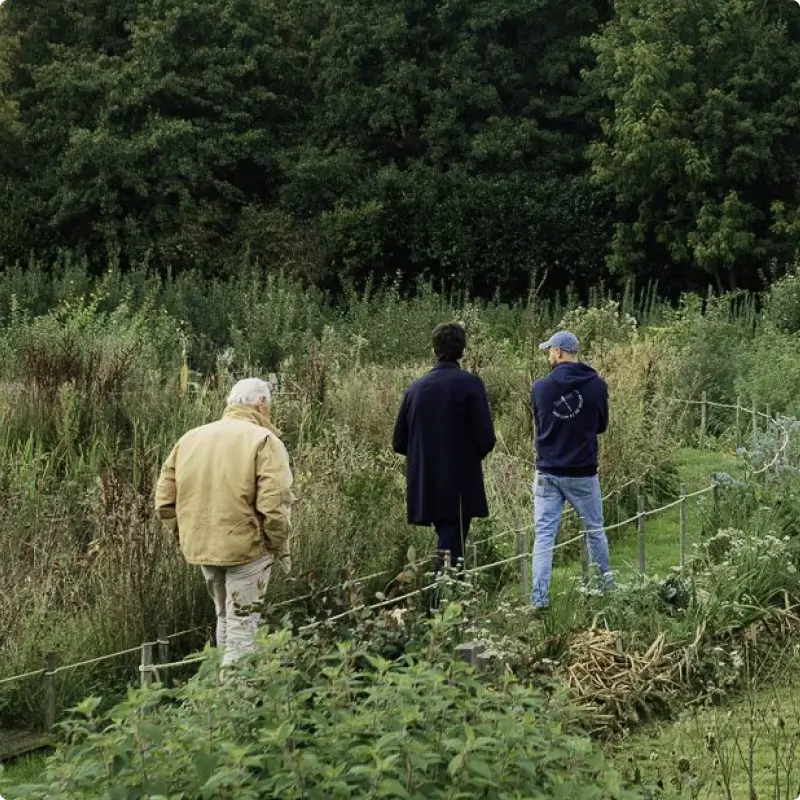 Yann Arthus-Bertrand et Tom Arthus-Bertrand se promenant au Jardin des Partages à la Vallée de la Millière, illustrant l'observation de la biodiversité sur cette parcelle en cours de réensauvagement.